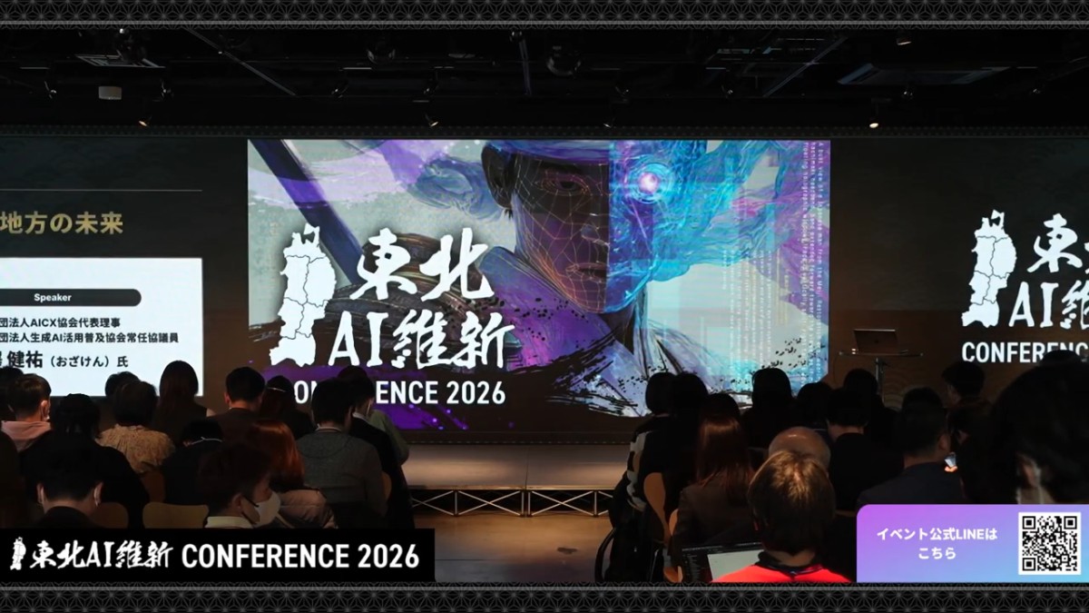 前回イベントのライブ配信画面。ステージの大型スクリーンに「東北AI維新 CONFERENCE 2026」のビジュアルが映り、手前の客席が埋まっている。画面下には配信のテロップが出ている。